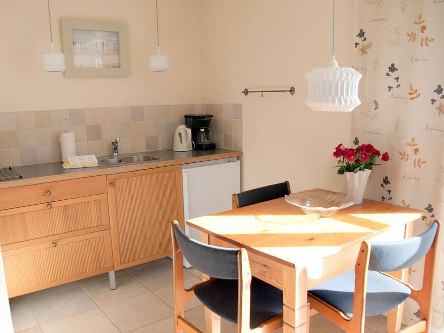 A kitchen with wooden cabinets, a sink, a coffee maker, and a dining table with chairs.
