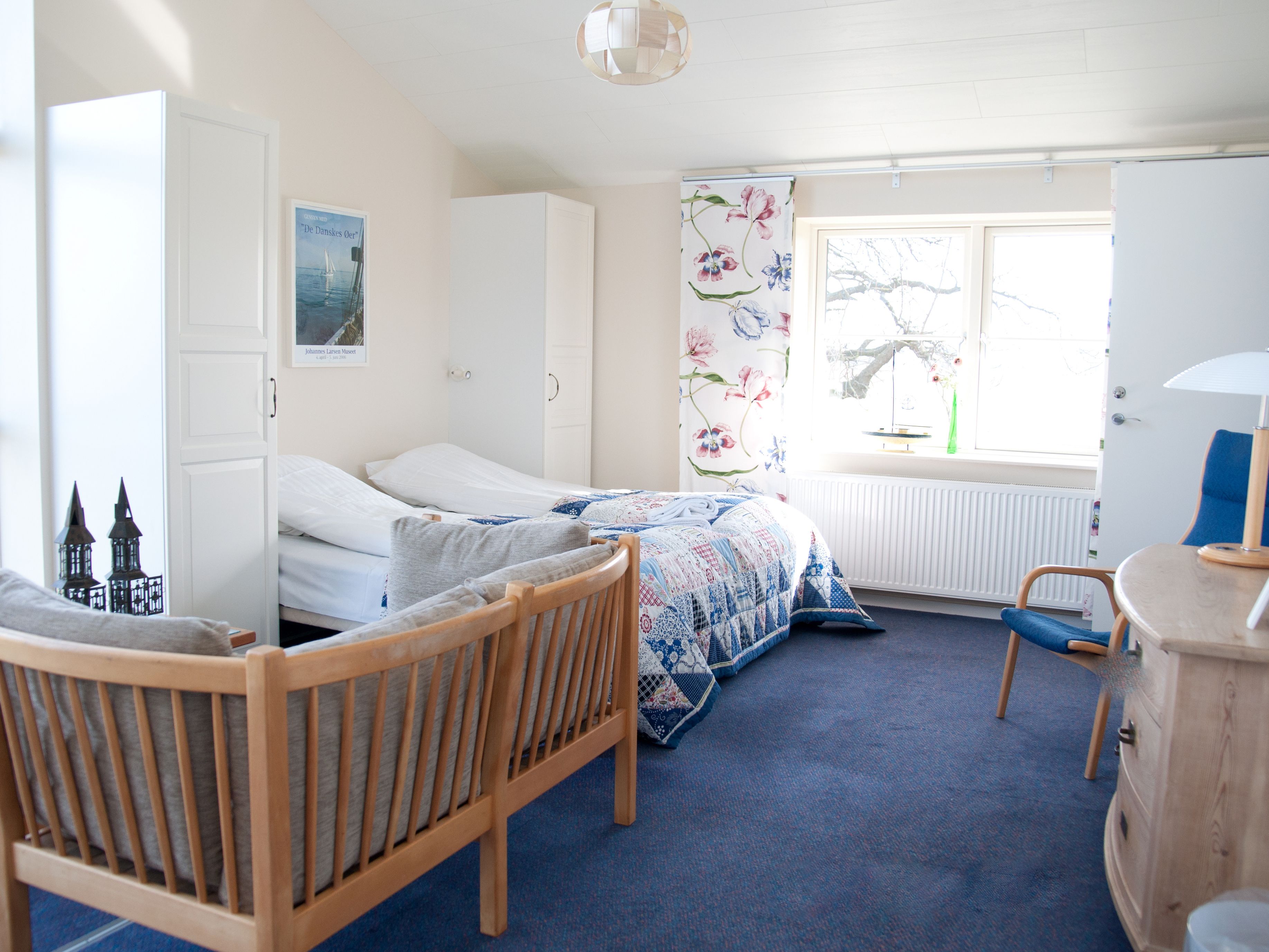 A bedroom with two single beds, a wooden chair, a dresser, a radiator, and a window with a view of trees.