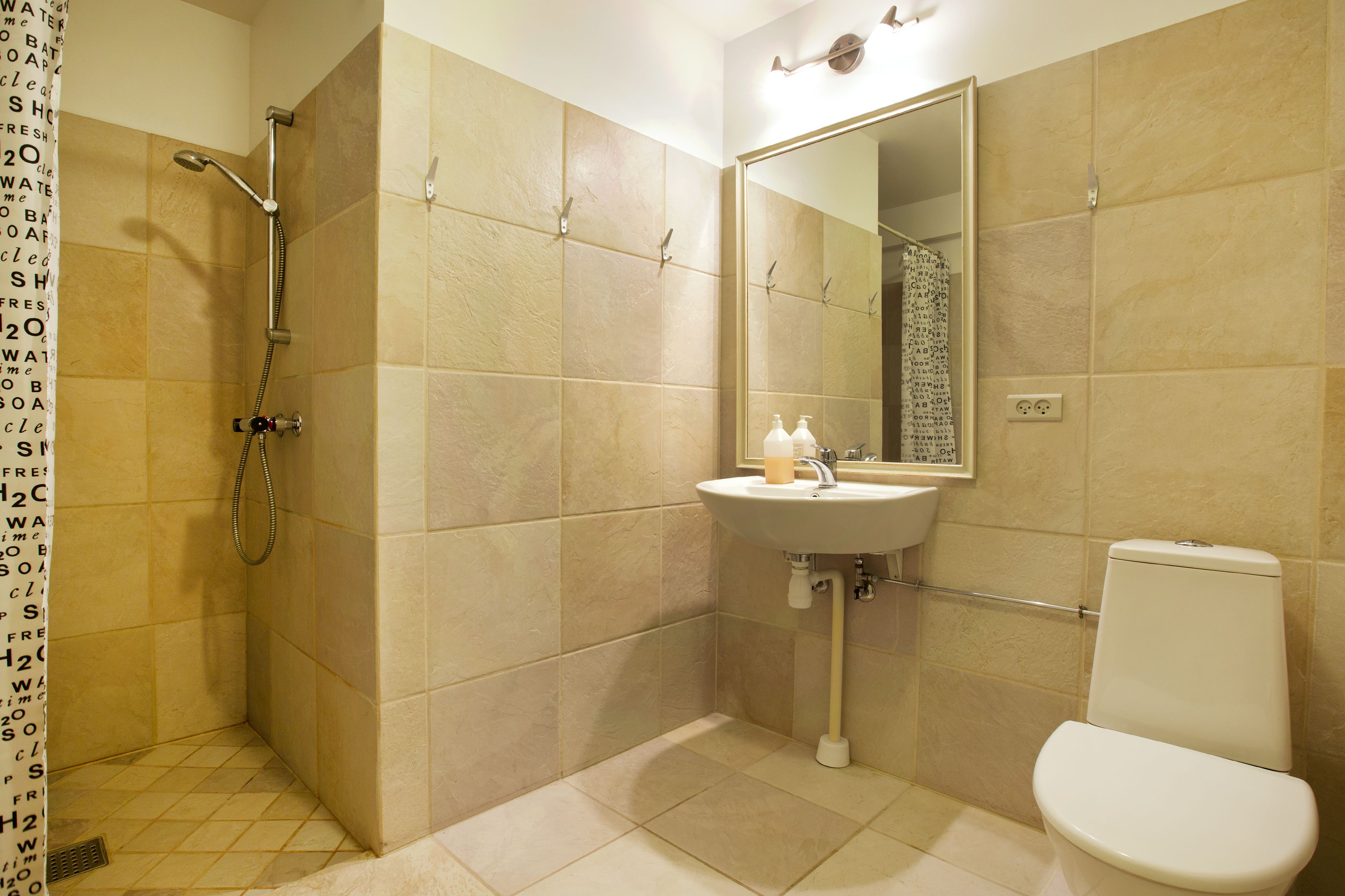 A bathroom with beige tiles, a shower, a sink, and a toilet.