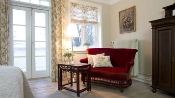 A room with a red velvet sofa, a wooden table, a radiator, and a window with floral curtains.