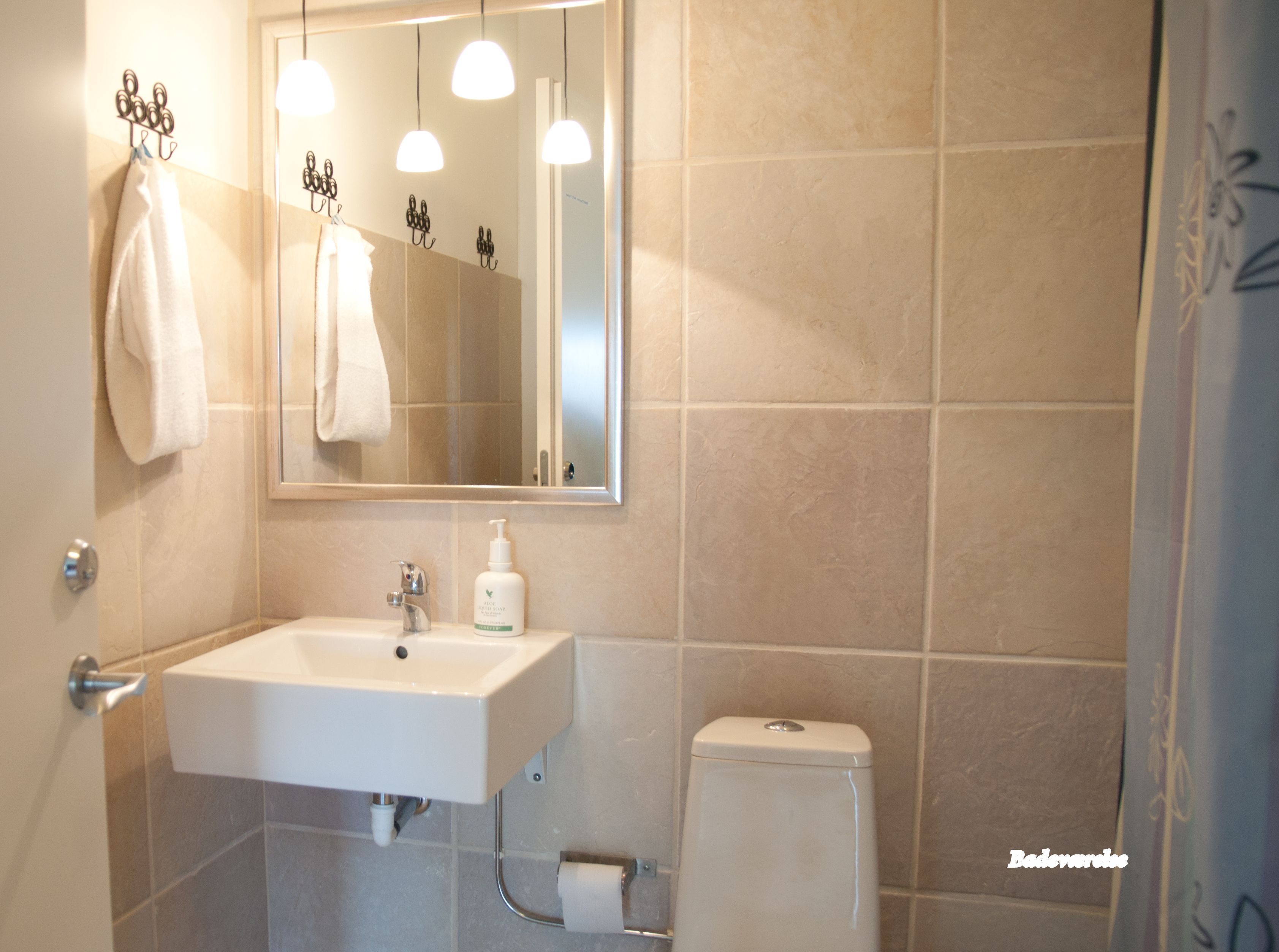 Un baño con lavamanos, espejo, toallero y retrete.