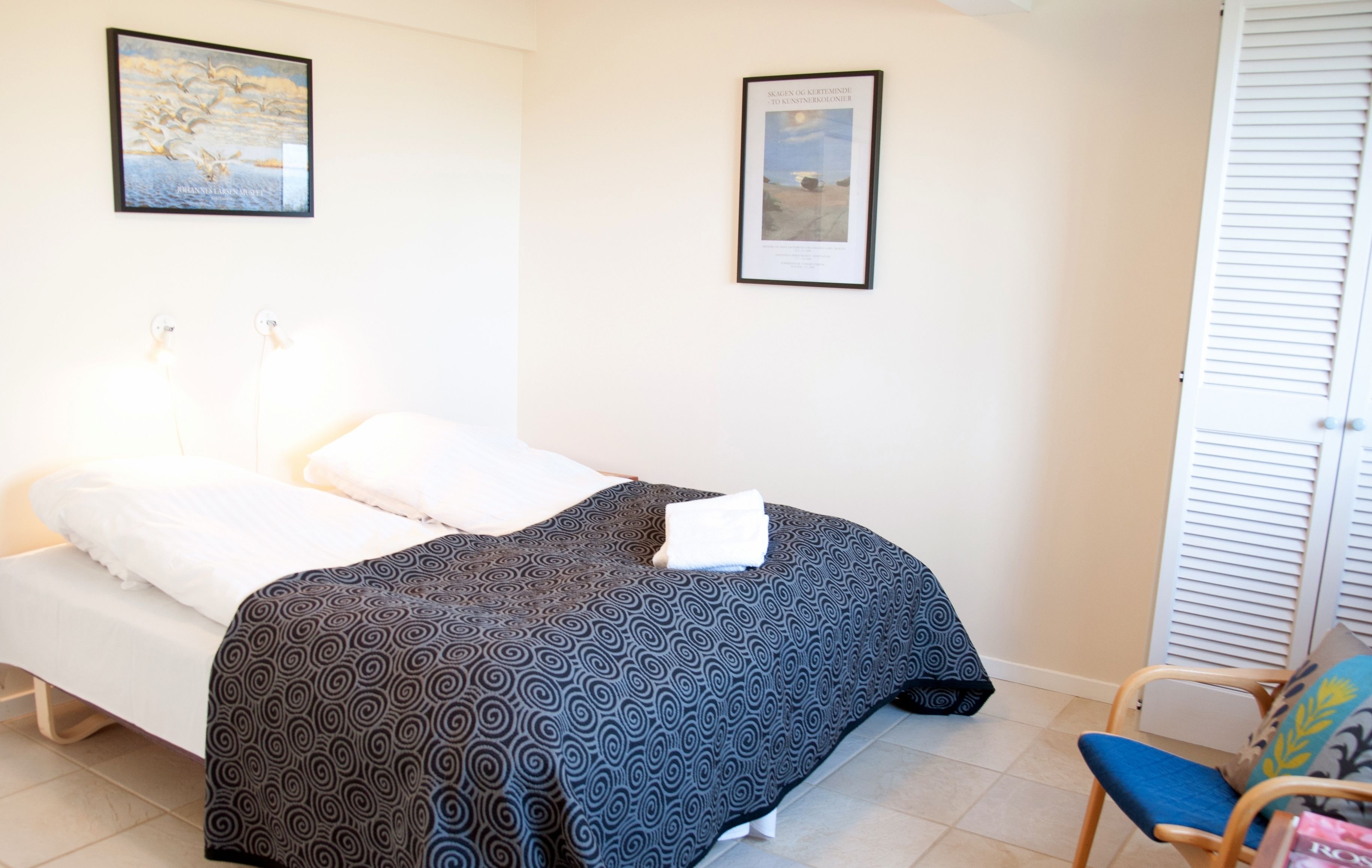 Une chambre à coucher avec un lit, une chaise et deux tableaux encadrés accrochés au mur.