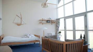 A room with a bed, a wooden chair, a small table, a lamp, and a large window.