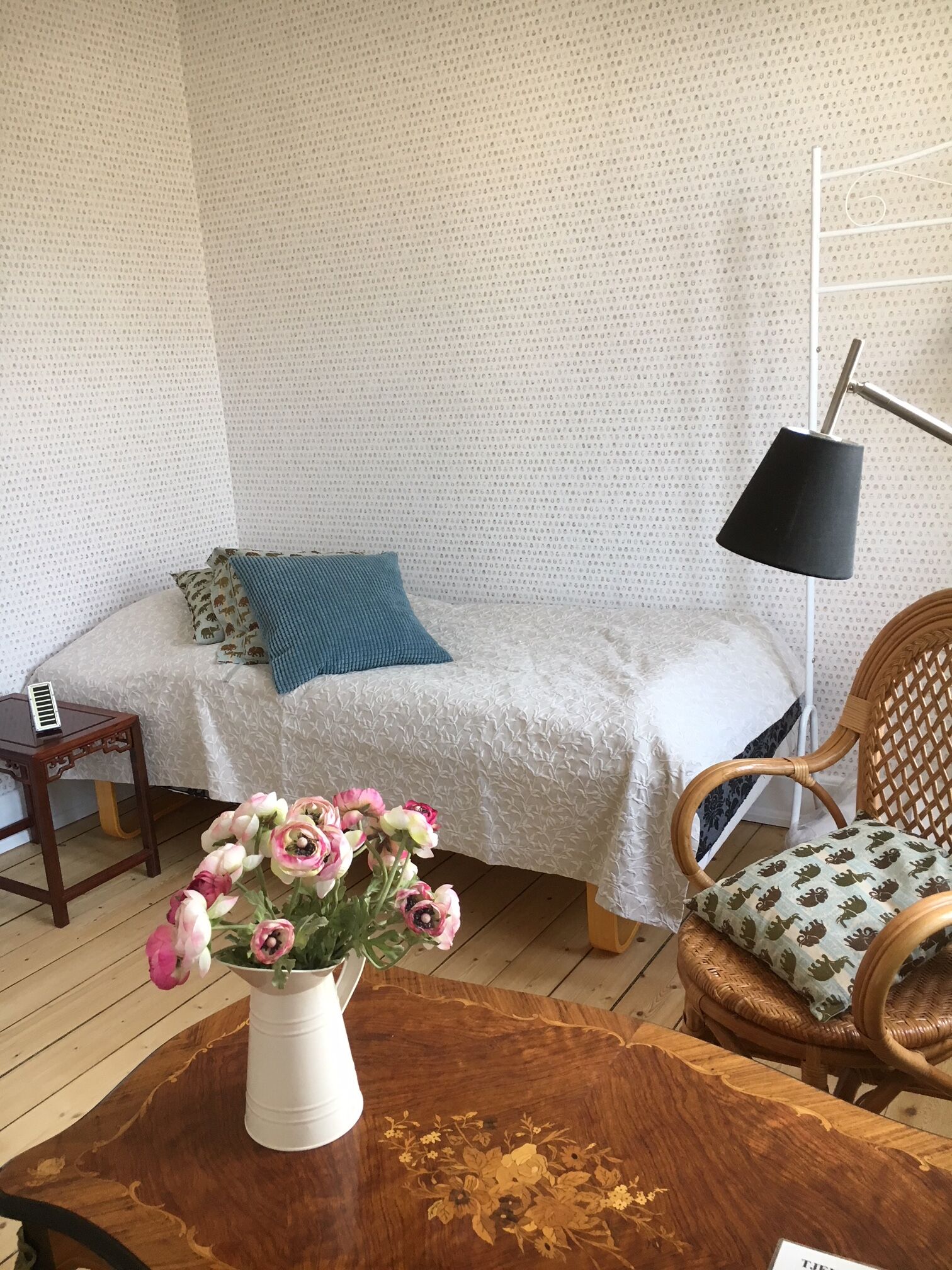 A cozy room with a bed, a bedside table, a lamp, a chair, and a wooden coffee table with a vase of flowers.