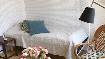 Una habitación acogedora con una cama, una mesita de noche, una lámpara, una silla y una mesa de centro de madera con un jarrón de flores.
