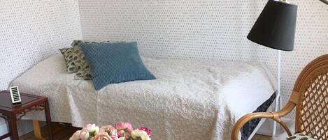 Una habitación acogedora con una cama, una mesita de noche, una lámpara, una silla y una mesa de centro de madera con un jarrón de flores.