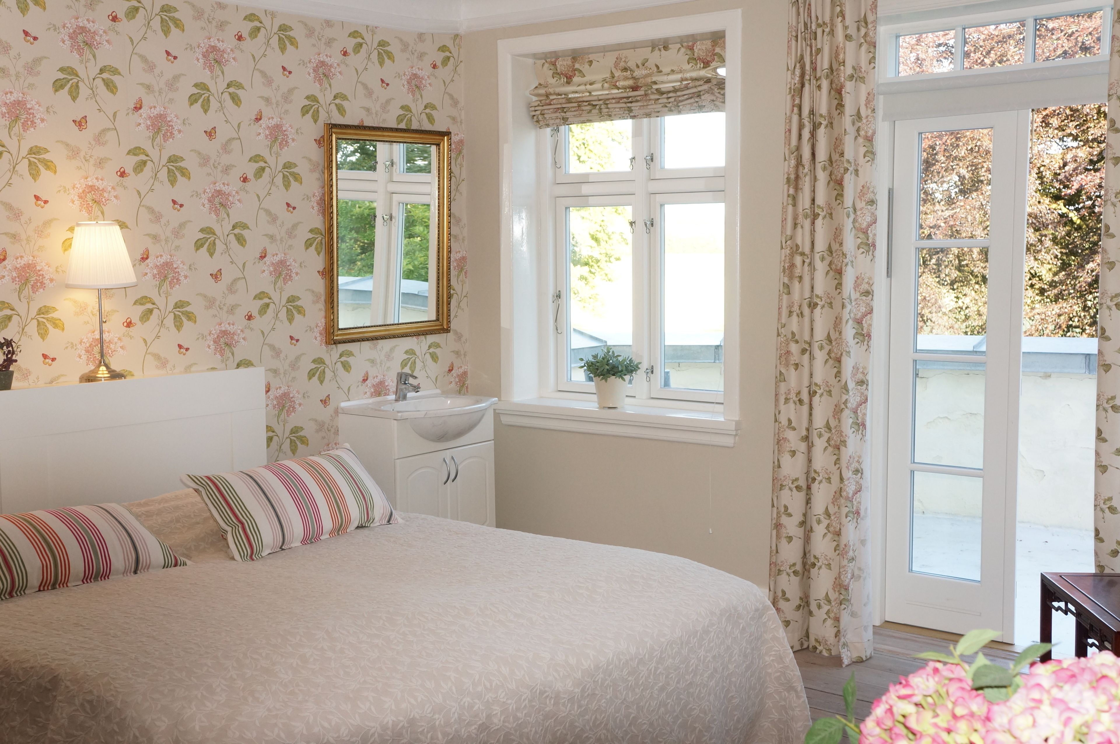 A bedroom with a bed, bedside table, lamp, and a window with curtains.