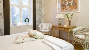 Une chambre à coucher avec un lit, deux chaises, une table, un vase de fleurs et un tableau encadré accroché au mur.