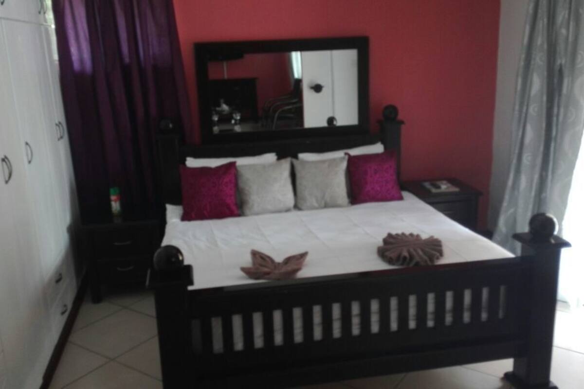 A bedroom with a bed, a nightstand, a dresser, and a mirror.