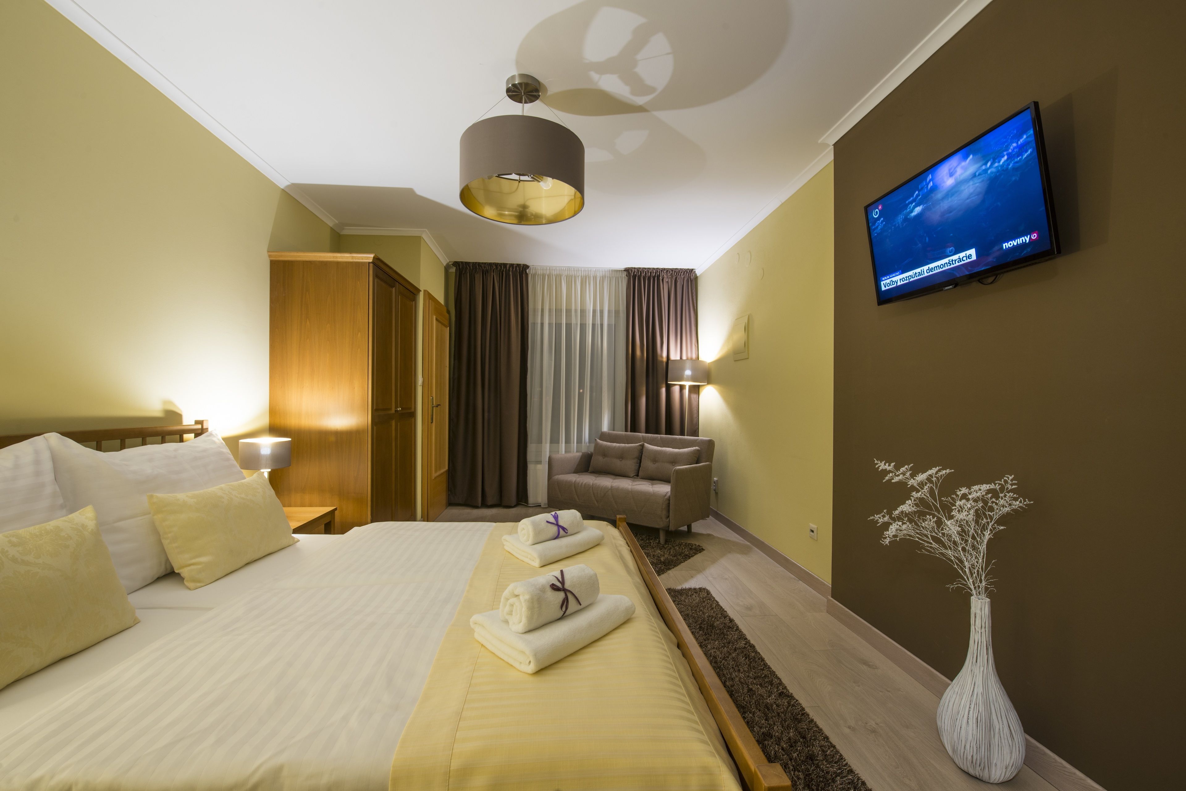 A hotel room with a bed, a TV, a sofa, and a vase.