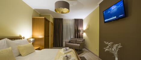 A hotel room with a bed, a TV, a sofa, and a vase.