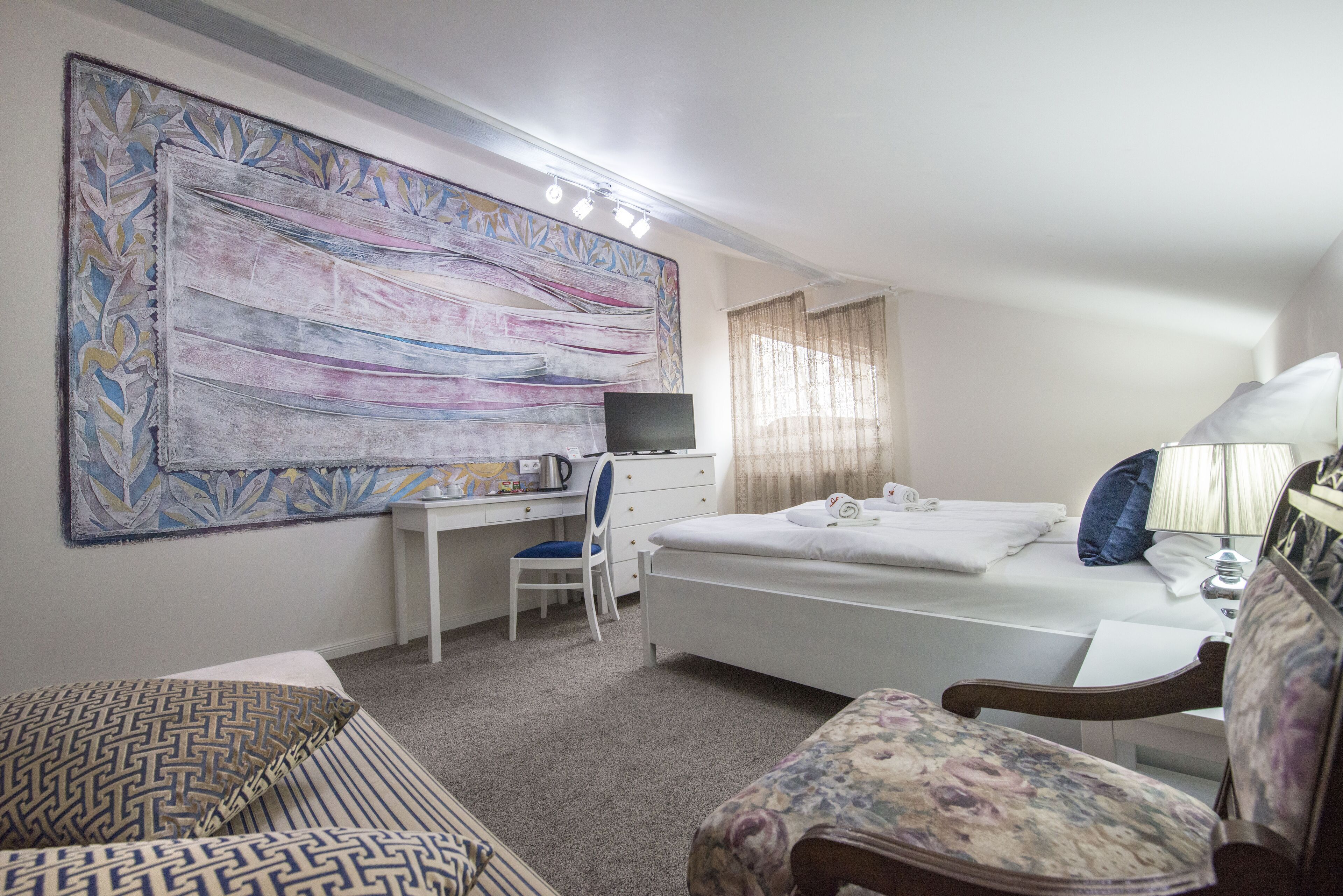 Habitación de hotel con cama, escritorio y silla, un cuadro abstracto grande y ventana con cortinas.