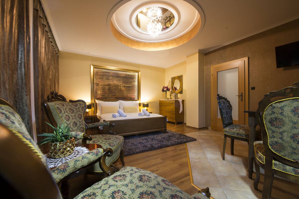 A hotel room with a bed, two chairs, a dresser, and a TV on the wall.