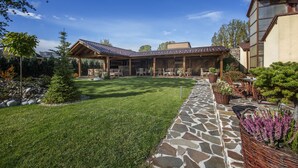 A covered outdoor patio with stone flooring, surrounded by a well-maintained lawn and potted plants.