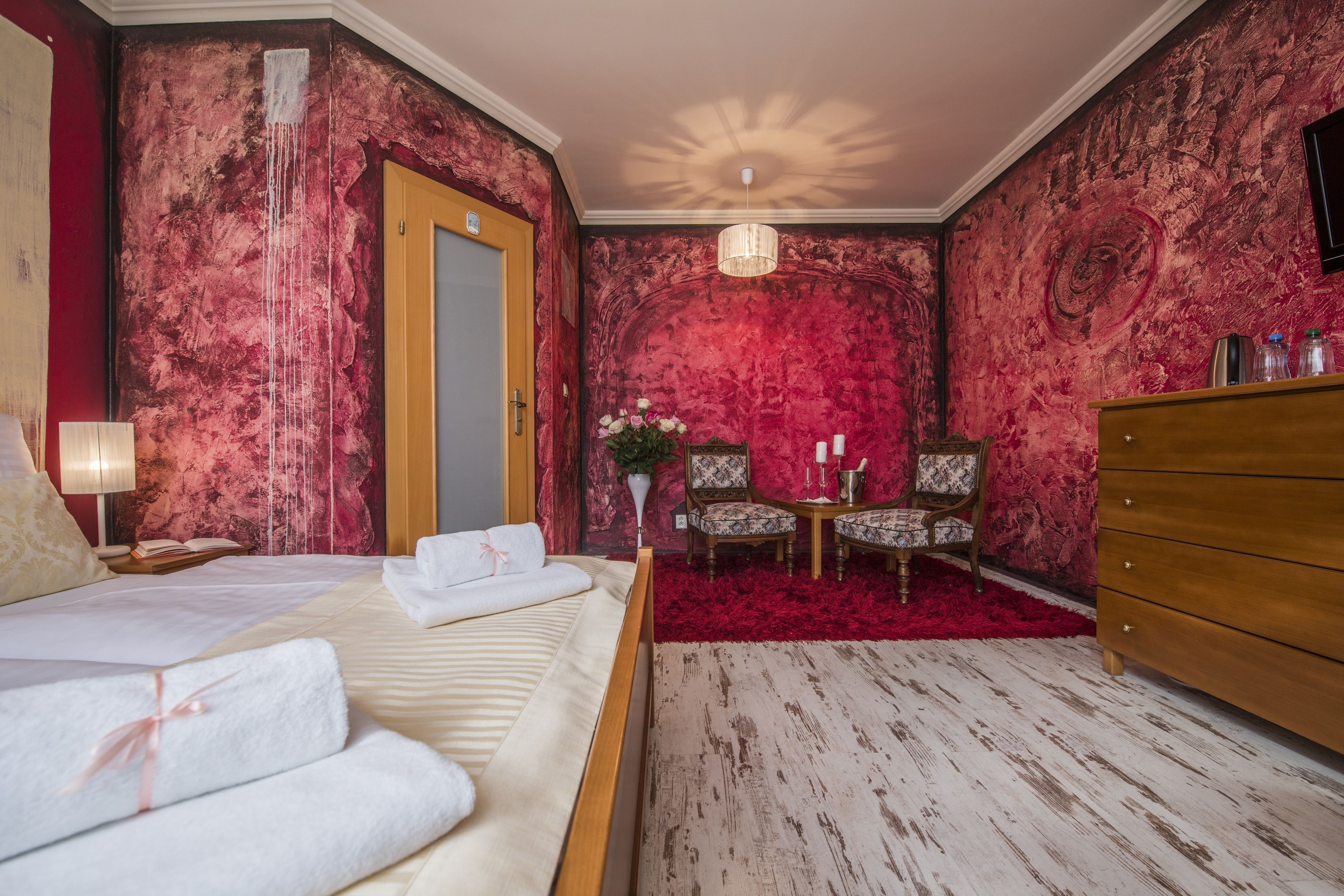 A bedroom with a bed, a dresser, a chair, and a small table with a vase of flowers.