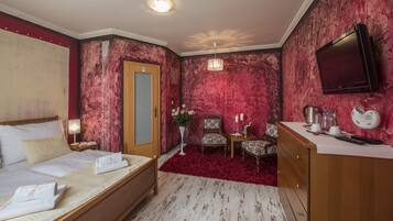 A hotel room with a bed, a wooden dresser, a television, and a red carpet.