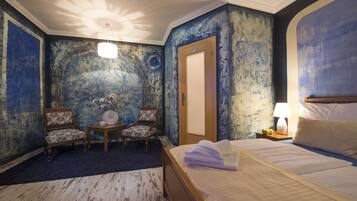 Habitación de hotel con una cama grande, un área de descanso con dos sillones, una mesita y una lámpara.