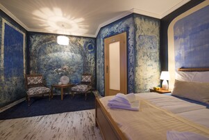Habitación de hotel con una cama grande, un área de descanso con dos sillones, una mesita y una lámpara.