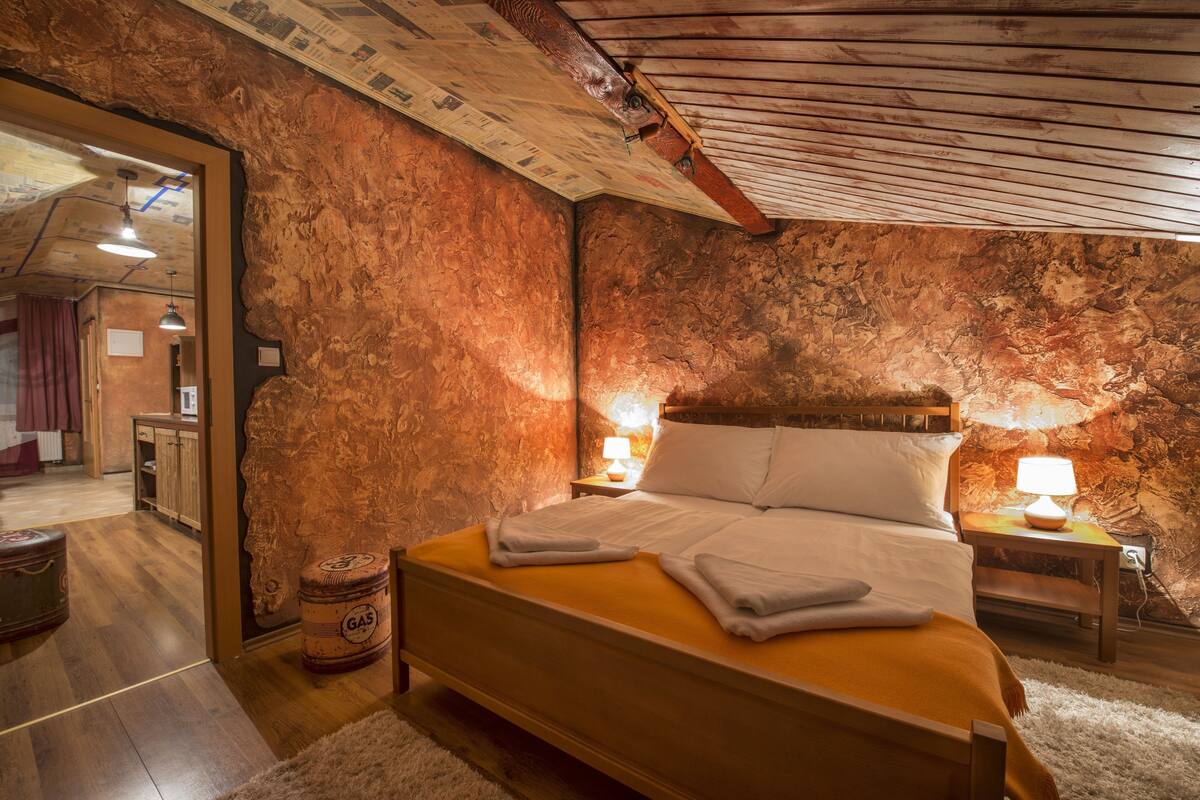 A bedroom with a wooden bed, two bedside lamps, a rustic wall, and a wooden ceiling.