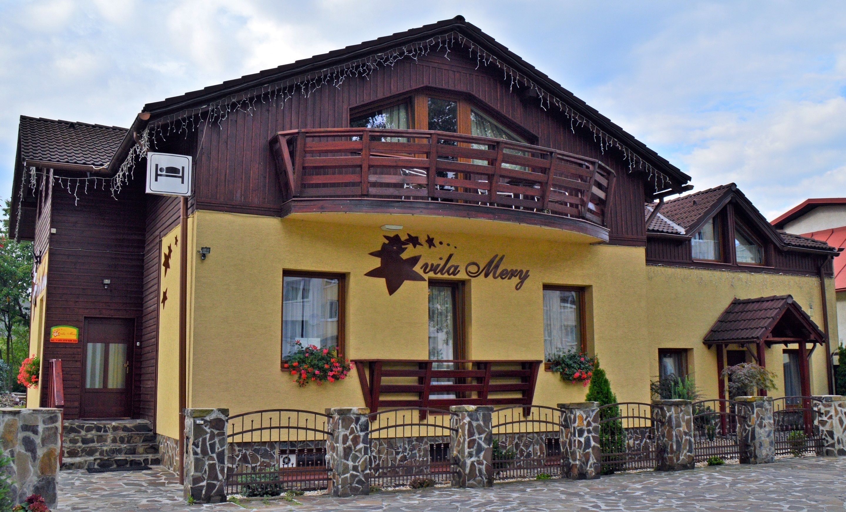 A building with a yellow facade, a wooden balcony, and a sign that reads "Vila Merry".