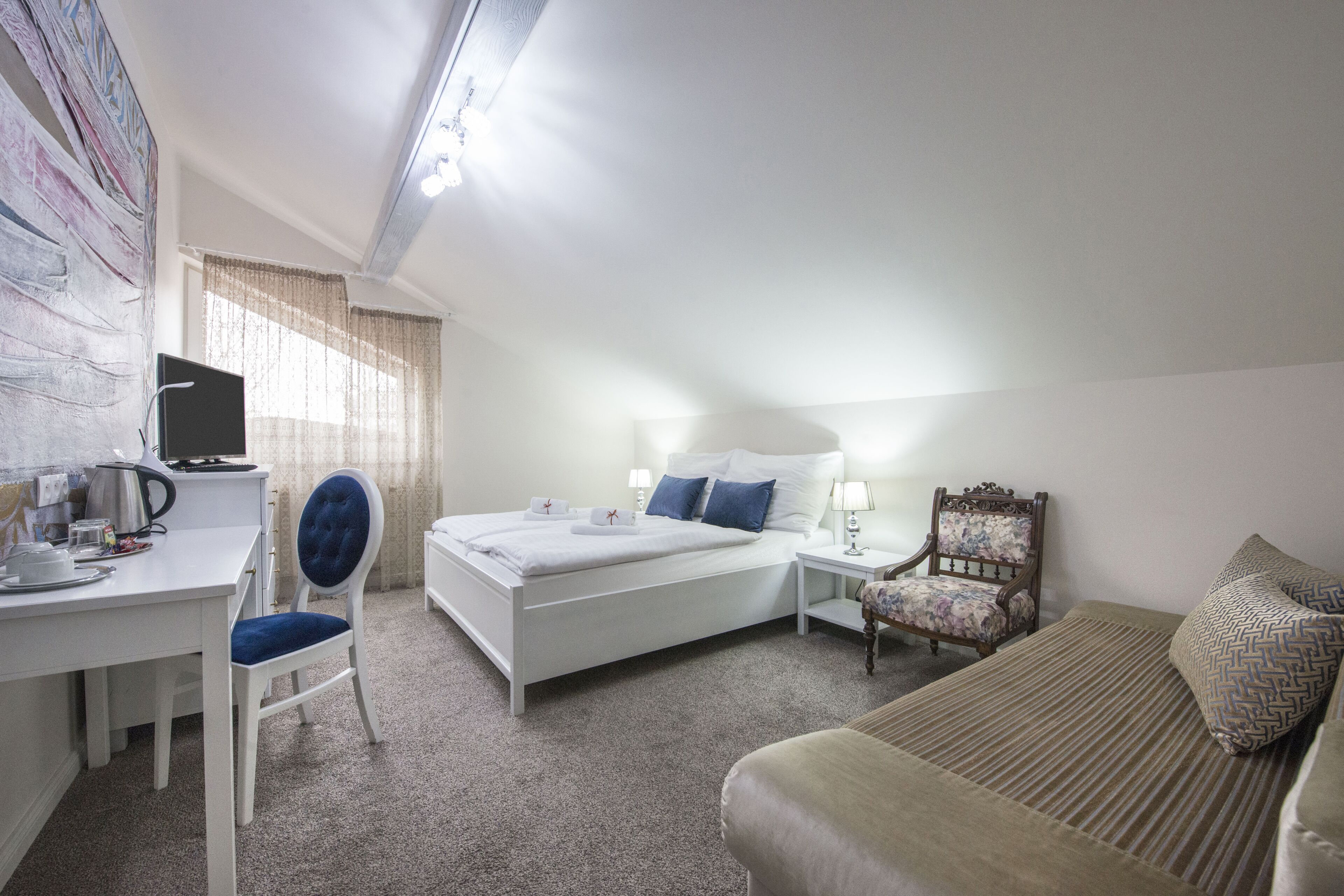 A hotel room with a bed, a desk with a chair, a small table, a chair, and a lamp.