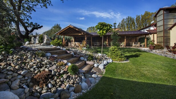 A well-maintained garden with a stone pathway leading to a wooden structure, surrounded by a lawn and trees.