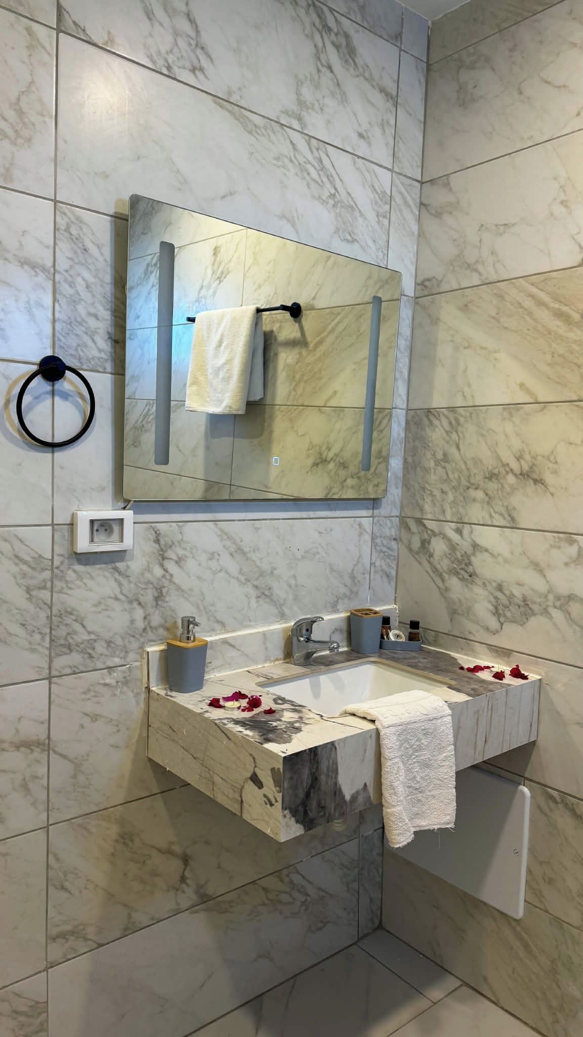 Un baño con pared de azulejos de mármol, un lavamanos con una toalla y un espejo encima.