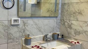 Un baño con pared de azulejos de mármol, un lavamanos con una toalla y un espejo encima.