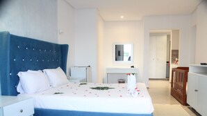 Ein Schlafzimmer mit einem großen Bett, einem Nachttisch, einer Kommode, einem Spiegel und einem kleinen Tisch mit Blumen in einer Vase.
