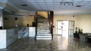 Eine großzügige Lobby mit einer Marmortreppe, einem Empfangstresen und einem modernen Deckenstil.