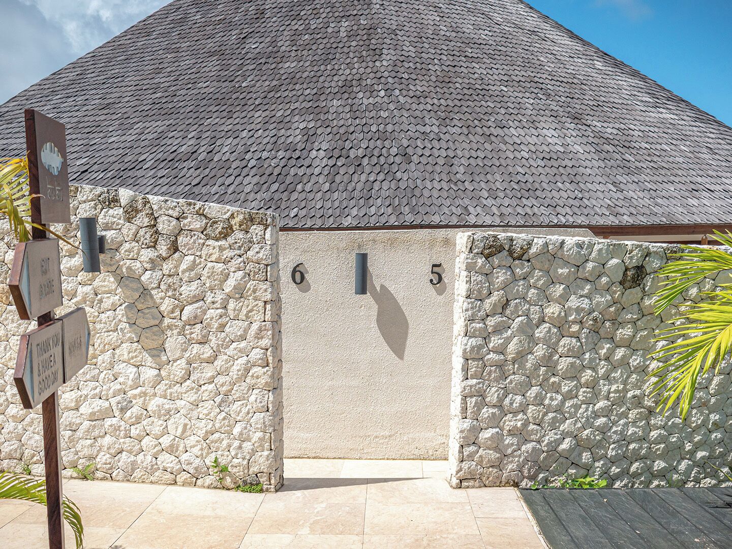 A building with a stone facade, a tiled roof, and a gate marked with numbers 6 and 5.