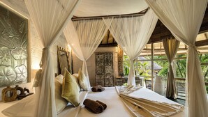 A bedroom with a canopy bed, a stone wall with floral carvings, and a view of greenery outside. - Biu Biu Resort Bali  (Jimbaran)