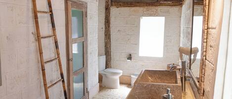 Un baño con un lavamanos de piedra, un inodoro, una escalera de madera y un ventanal grande.