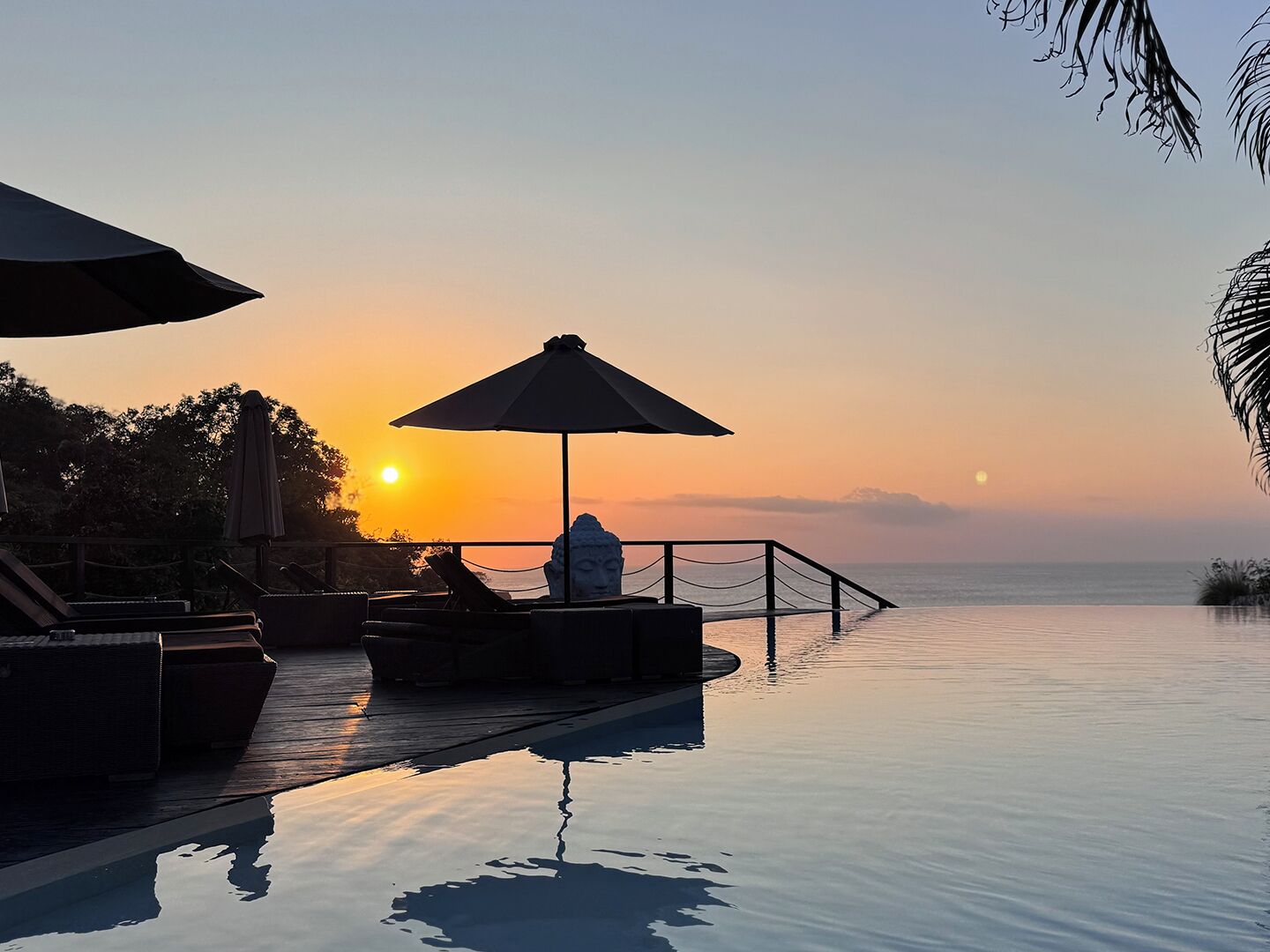 A serene sunset view from an infinity pool with lounge chairs and umbrellas.