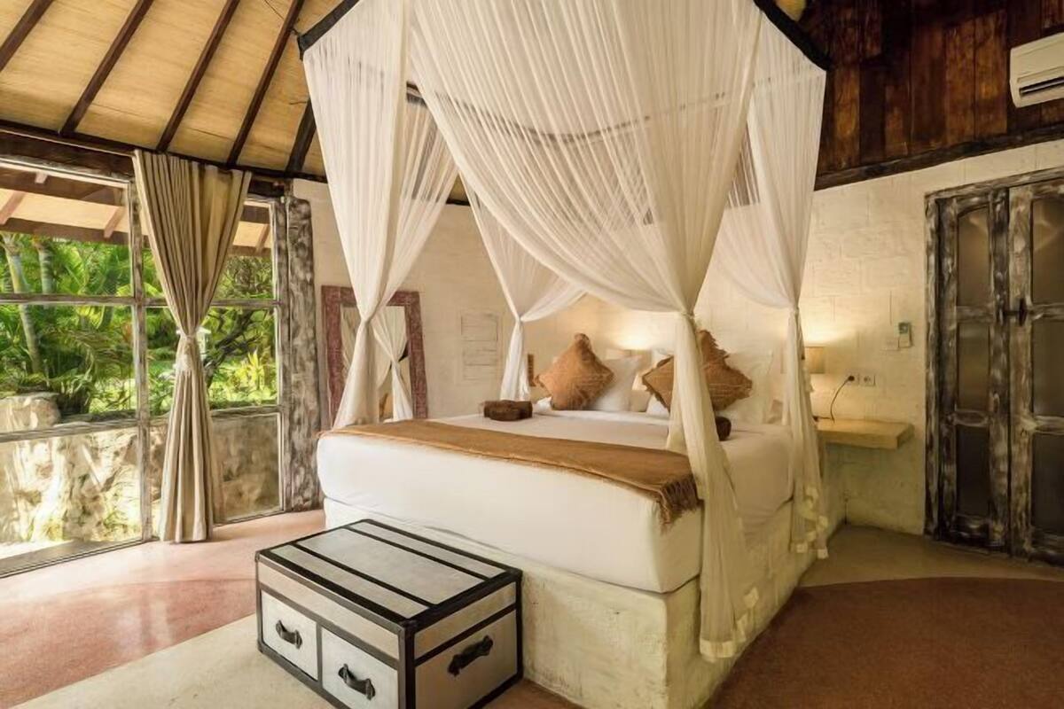 Een bed met hemelbed, een nachtkastje en uitzicht op groen.