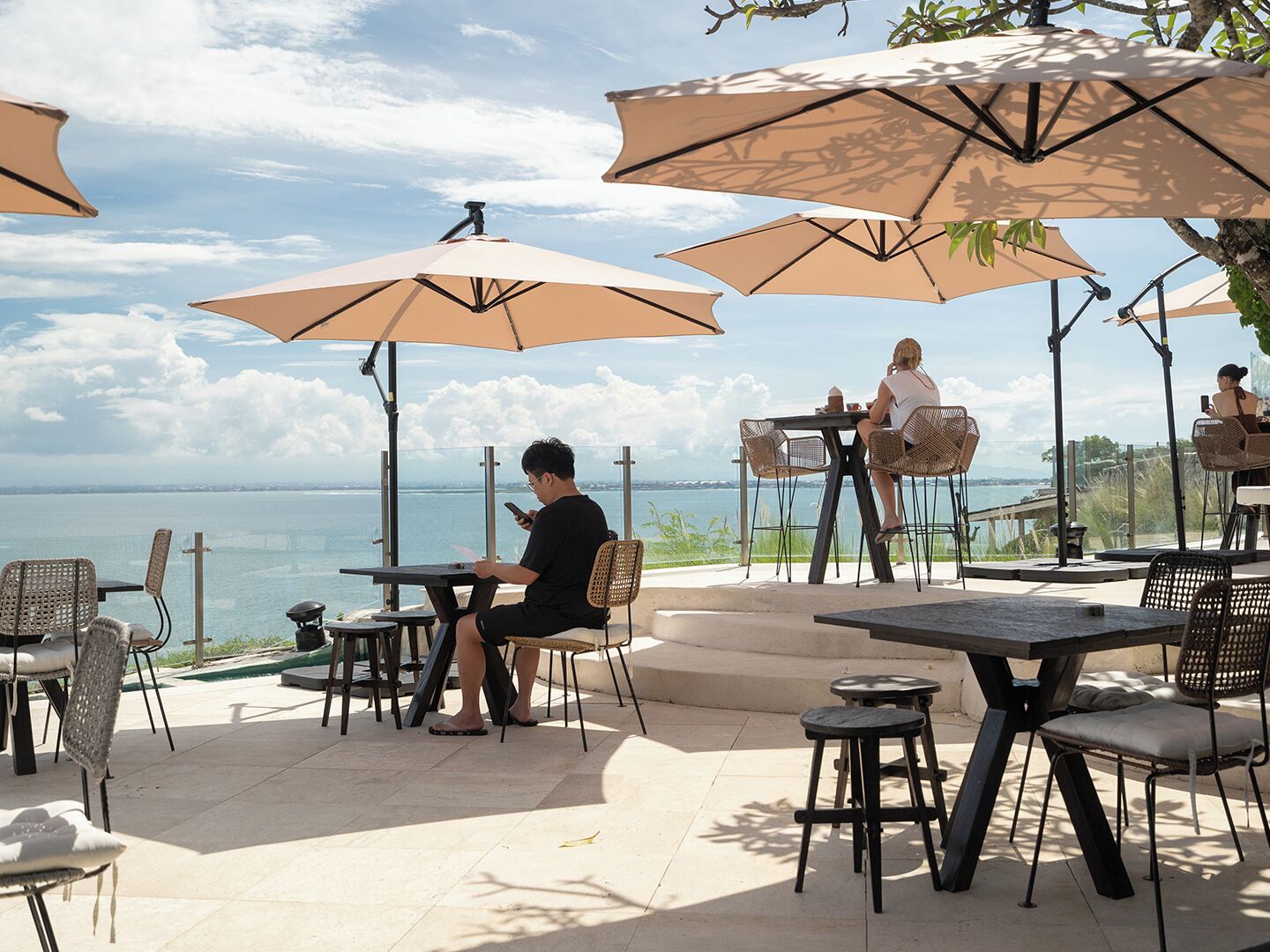 Un espacio al aire libre con mesas y sillas, sombrillas y vista al mar.