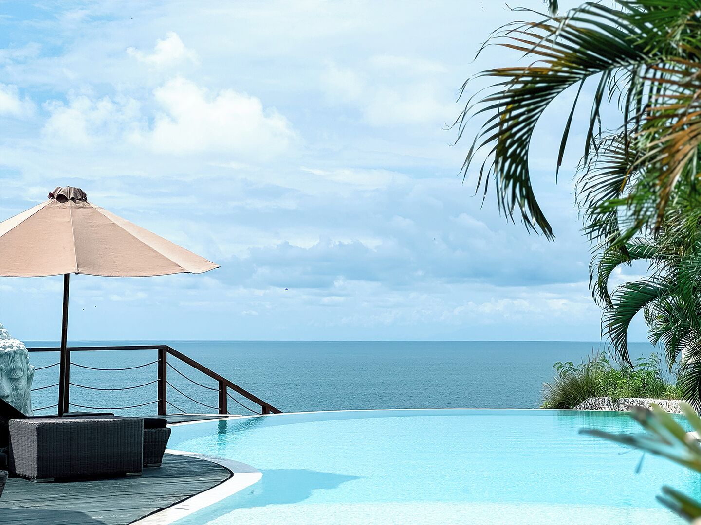 A pool with a view of the sea, a lounge chair, and a beach umbrella.