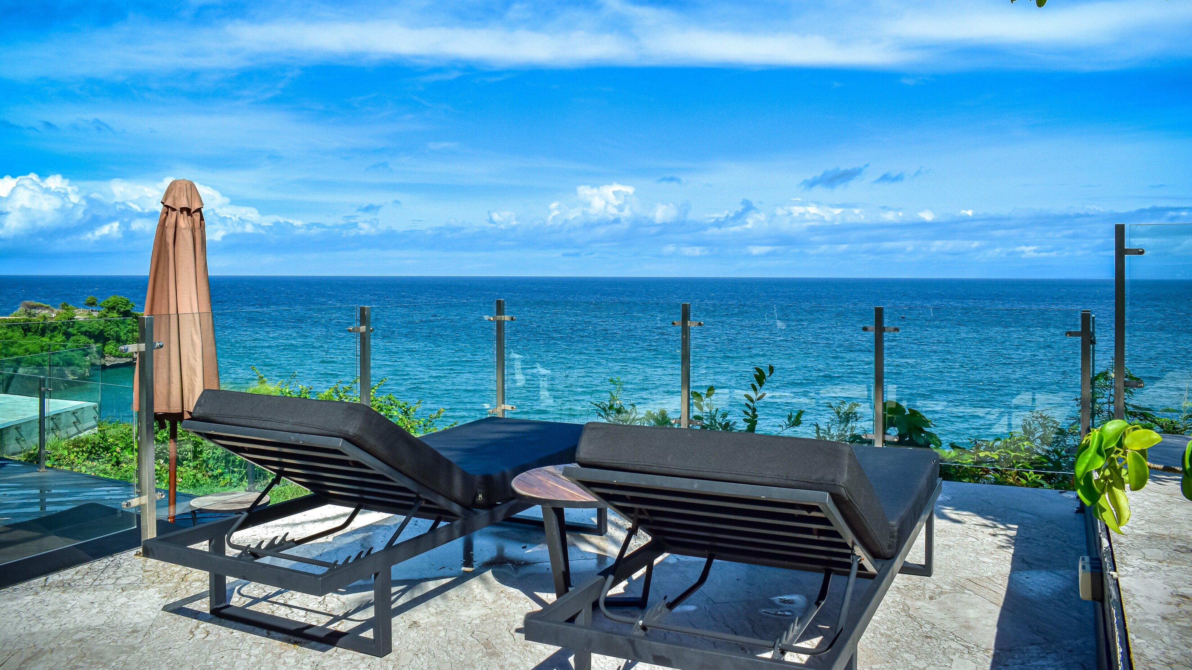 A patio with two lounge chairs and an umbrella, overlooking a coastal view.