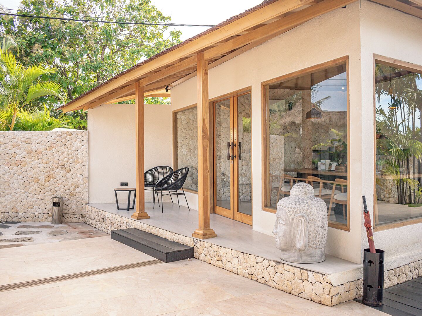 A covered outdoor seating area with stone walls, a statue, and a thatched roof structure.