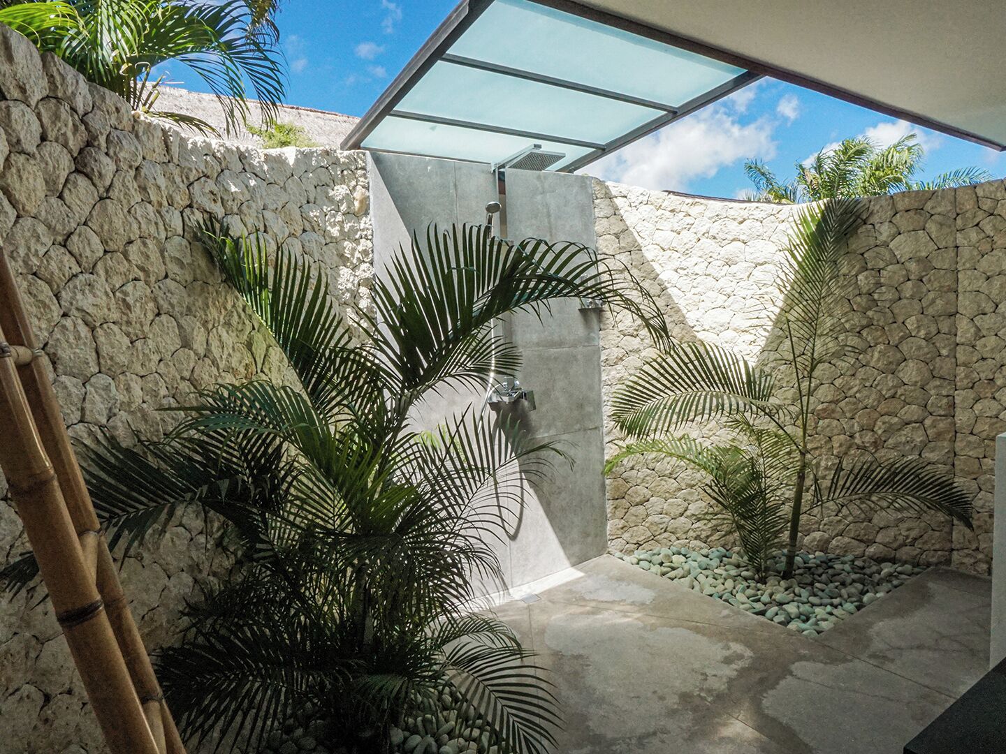 Un espacio exterior moderno con pared de piedra, palmeras y techo de vidrio.