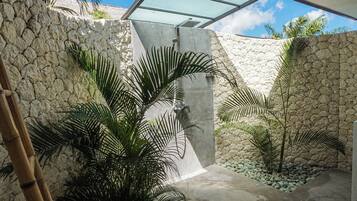 Un espacio exterior moderno con pared de piedra, palmeras y techo de vidrio.