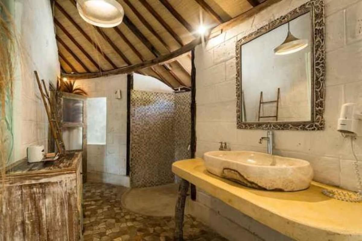A rustic bathroom with a stone sink, wooden ceiling, and a mirror with an ornate frame.