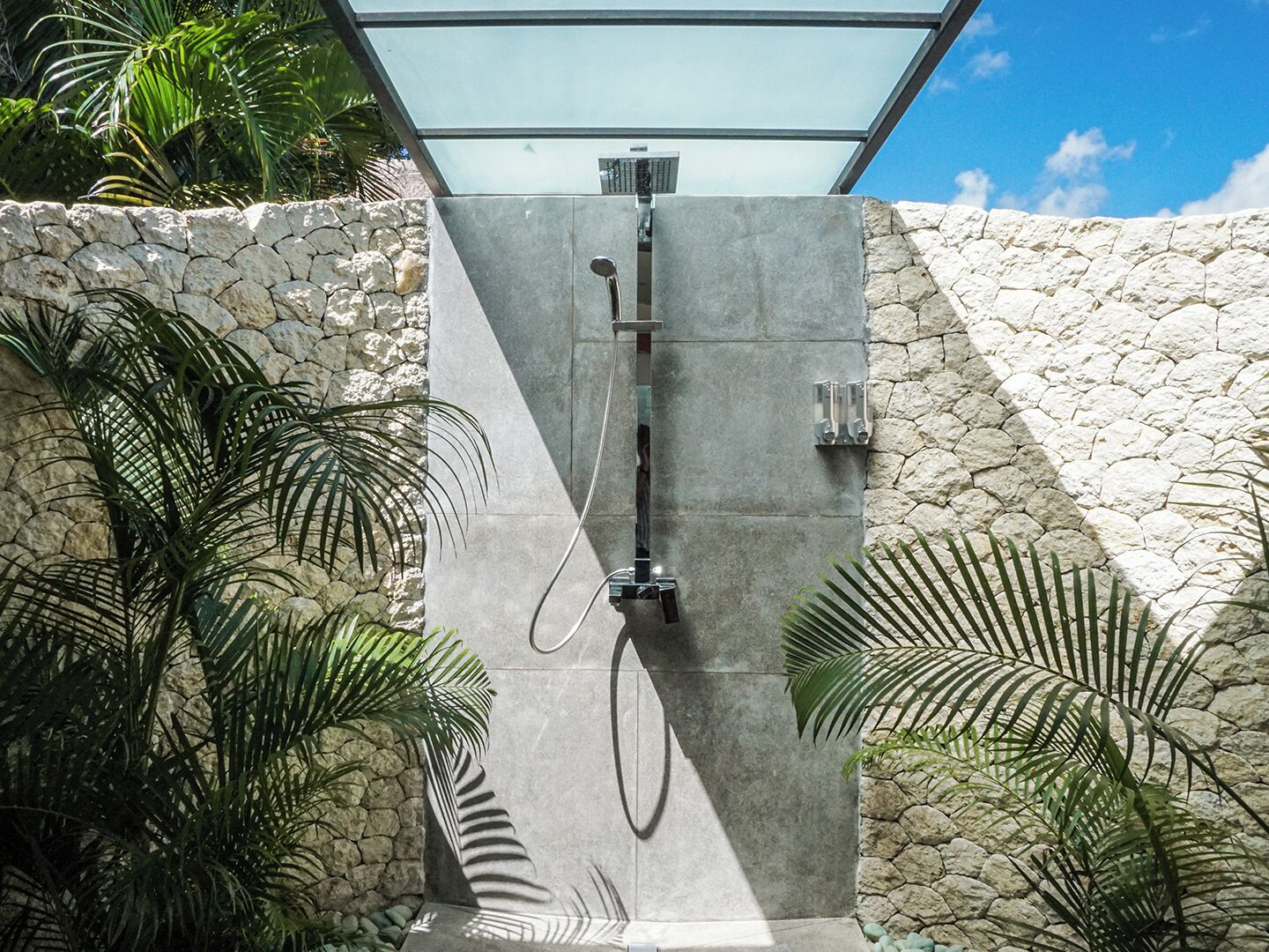 Un espace de douche moderne avec un mur en pierre en arrière-plan et une végétation tropicale.