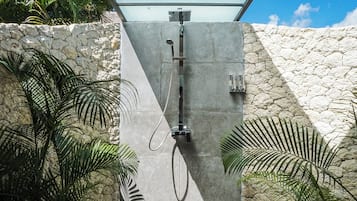 Un espace de douche moderne avec un mur en pierre en arrière-plan et une végétation tropicale.