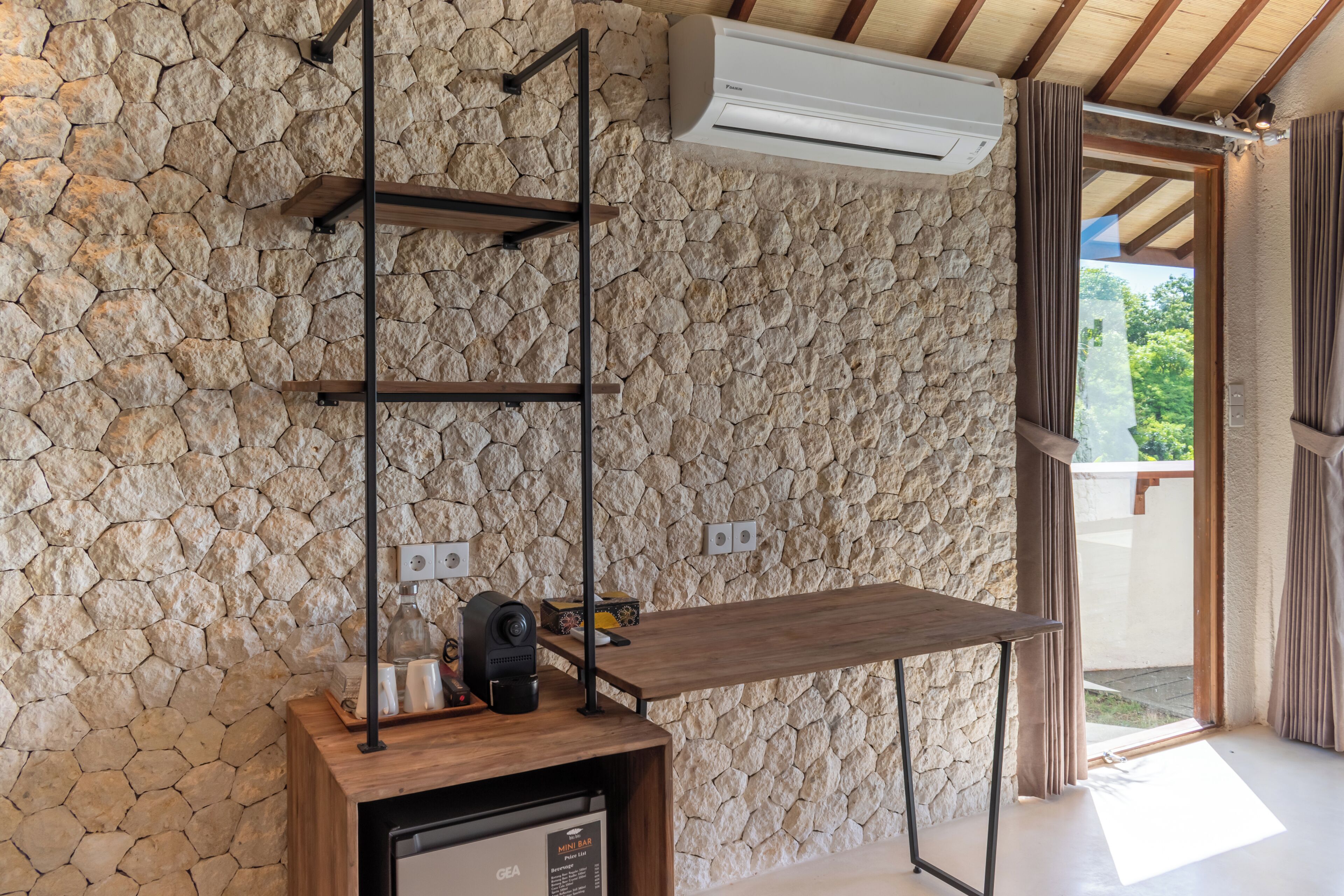 A room with a stone wall, a wooden shelf with a coffee maker, and a mini fridge.