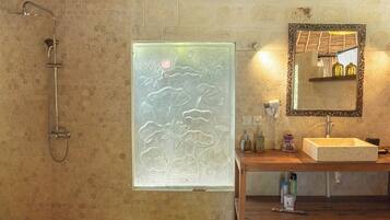 A bathroom with a shower, a glass door with floral patterns, a wooden vanity with a sink, and a mirror with a decorative frame.