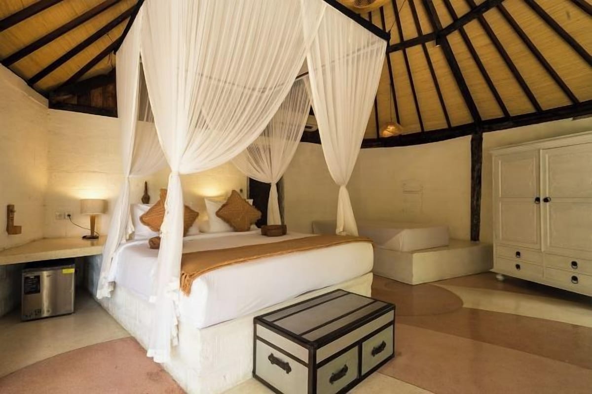 A bedroom with a canopy bed, bedside tables, a wardrobe, and a small seating area.