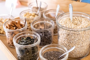 A variety of food items in glass jars, including nuts, seeds, and grains, arranged on a wooden surface. - Albergo Palazzo Lodron Bertelli (Caderzone Terme)