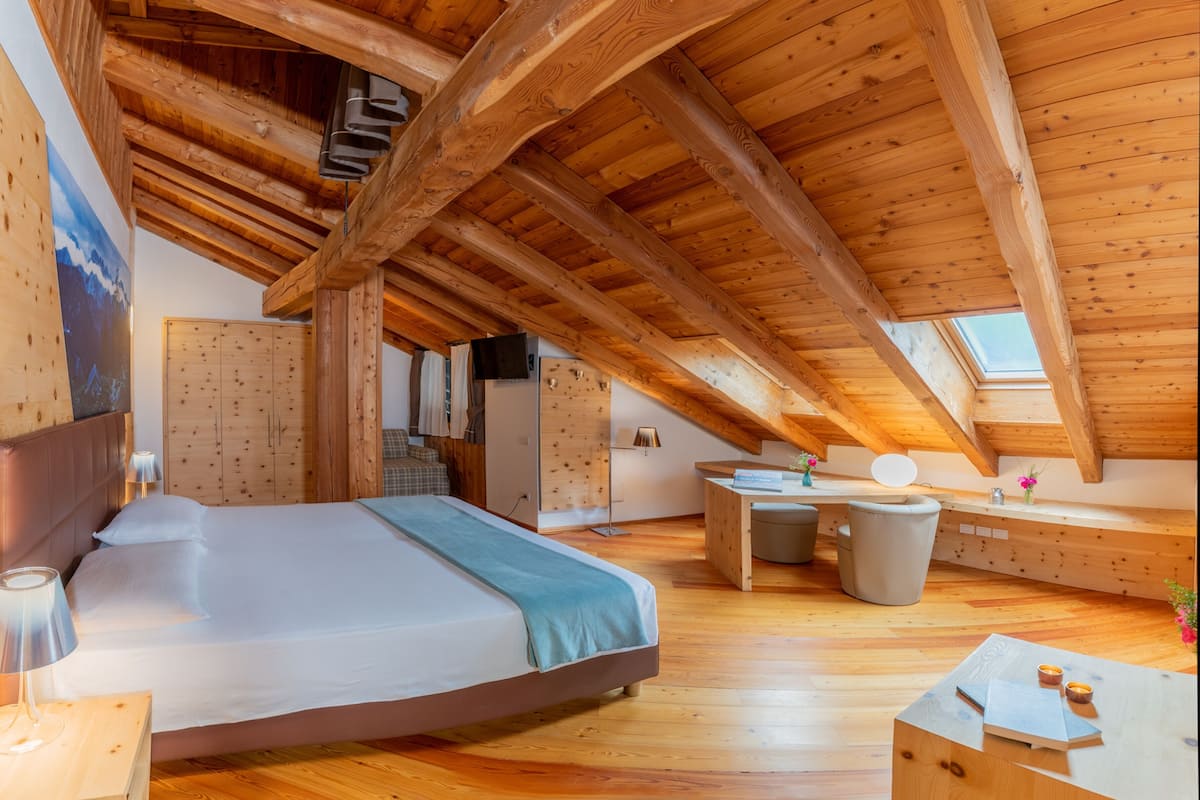 A cozy attic bedroom with a wooden ceiling, a large bed, a desk, and a window.
