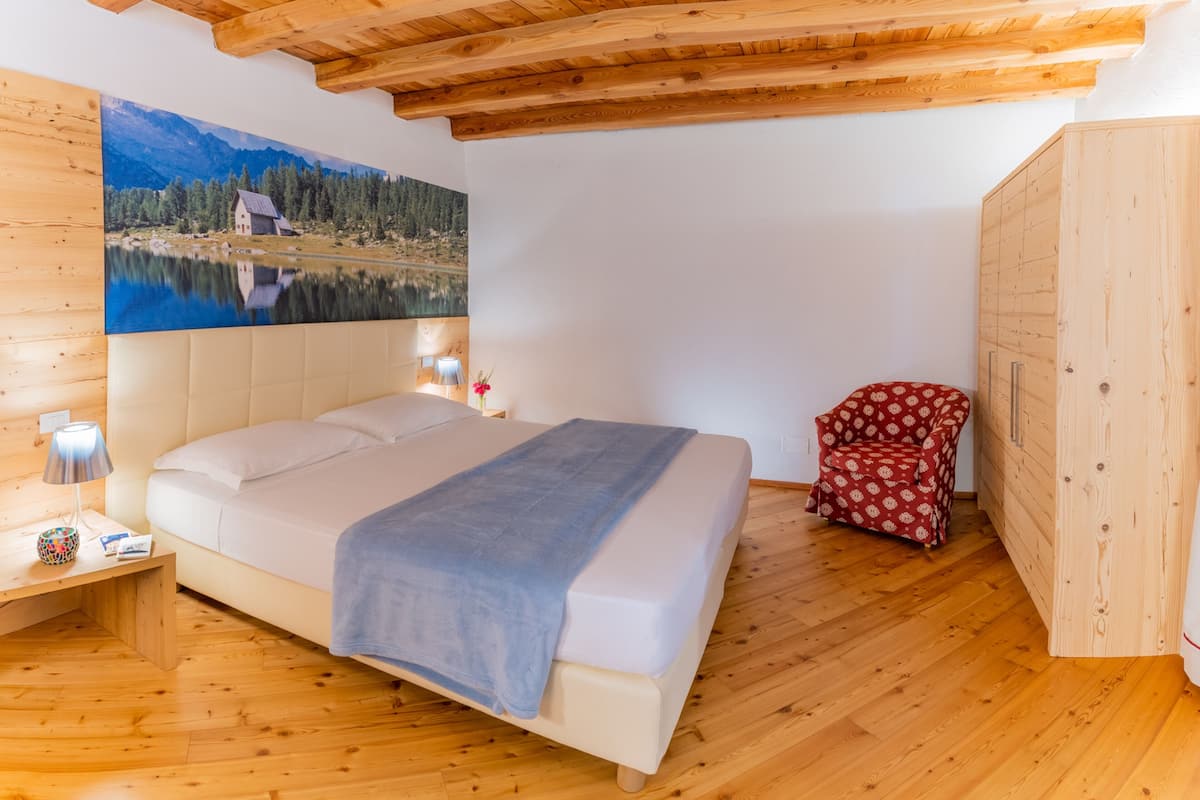 A bedroom with a bed, wooden floor, a painting of a lake, a nightstand, and a wardrobe.